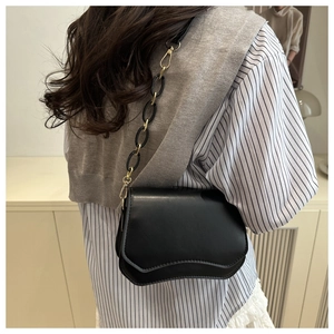 Detail of black crossbody bag featuring a unique wavy flap and mixed gold chain strap