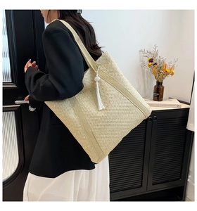 Detail view of a large woven straw tote bag with tassels on a fashion model