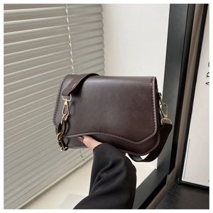 Detail of dark brown leather crossbody bag with wave edge design and gold chain strap