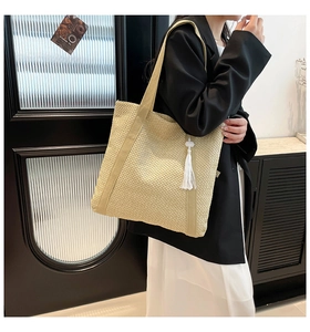 Detailed close-up of beige knitted tote bag with white tassel and woven texture