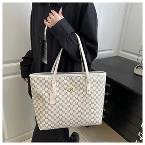 Close-up of cream tote bag with dark grey M print and gold metal logo on black shirt