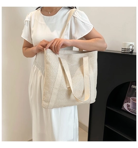 Detail of a large cream woven tote bag with textured tassels and wide fabric straps