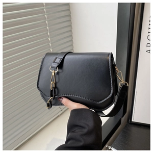 Detail of black leather crossbody bag featuring unique wavy curved bottom and gold chain