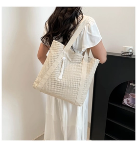 Detailed view of a large woven tote bag with a white tassel worn by a model in a minimalist room