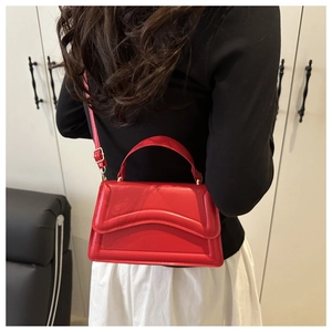 Detail of red leather crossbody bag with wavy flap shown on shoulder for size