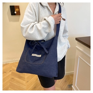 Détail du sac cabas en jean bleu avec poche décorative et étiquette tissée blanche