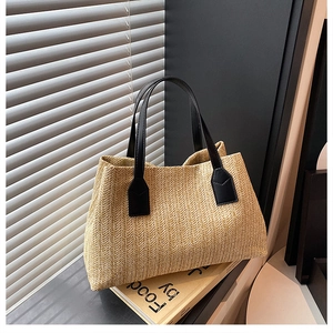 Close-up of woven straw tote bag featuring contrast black leather handles and reinforced base