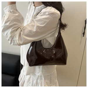 Close-up of a dark brown glossy patent leather hobo bag worn on a white lace shirt
