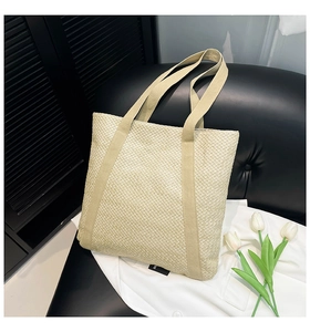 Détail d'un sac cabas en paille tissée beige posé sur une chaise en cuir noir chic