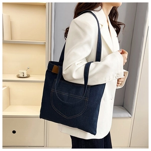 Detail of dark blue denim tote bag with yellow contrast stitching and leather side patch