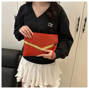 Detail of red envelope clutch bag with woven texture and gold V-shaped metal trim