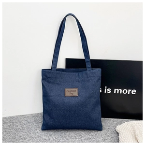 Détail d'un sac cabas en denim bleu foncé avec un patch en cuir marron et deux anses