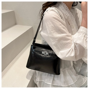 Detail of black glossy tote bag with silver metal turn-lock closure on white blouse