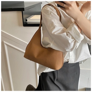 Close-up of brown crescent underarm bag with unique woven texture on white shirt