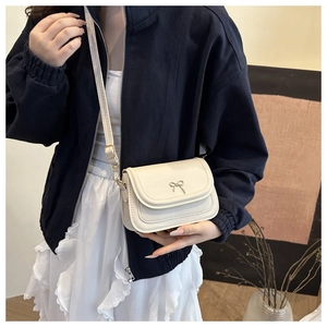 Detail of cream white crossbody bag with elegant metal bow buckle and flap closure