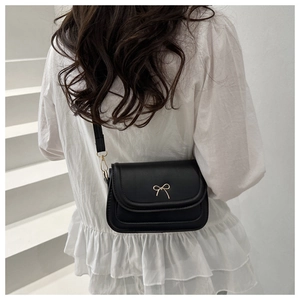 Close-up of black crossbody bag with gold bow clasp on female model back view