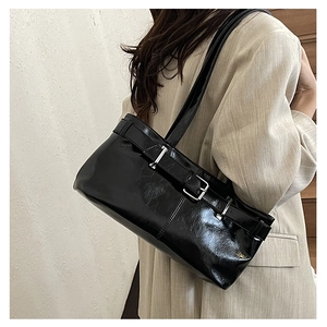 Model wearing black patent leather baguette bag with buckle straps and minimalist suit