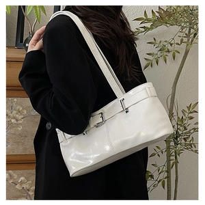 Close-up of minimalist white shoulder bag with metallic buckle on black blazer background