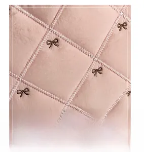 Gros plan sur tissu matelassé rose avec broderies de nœuds bruns et coutures en losange