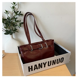 Close-up of wine red glossy leather underarm bag with belt detail in a display box