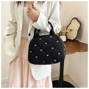 Détail d'un sac à main noir matelassé avec motif nœud blanc, porté par un mannequin