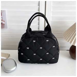 Détail d'un sac à main matelassé noir avec motif de nœuds blancs et fermeture éclair