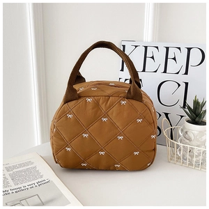 Gros plan du sac fourre-tout matelassé caramel avec broderie de nœuds blancs et surpiqûres