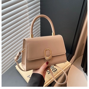 Close-up of beige square handbag with gold metal lock and elegant top handle detail