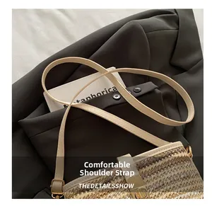 Detail of adjustable cream faux leather strap and golden buckle on woven straw bag