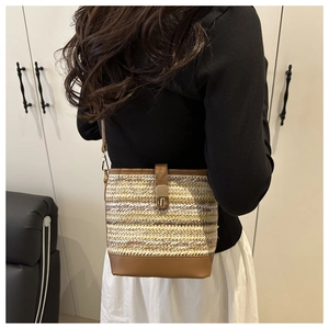 Détail d'un sac seau en paille tissée avec bordure en cuir marron et fermoir doré