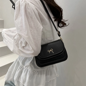 Minimalist black square crossbody bag with gold bow clasp worn with white ruffled top