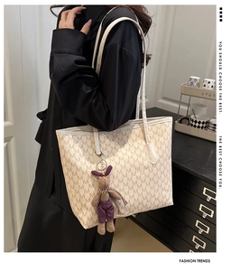 Side view of cream letter-print tote bag with a small rabbit charm on long leather strap