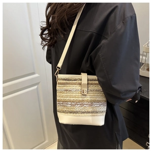 Detail of woven bucket bag featuring cream leather strap and gold metal buckle closure