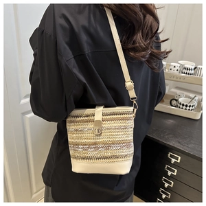 Détail du sac seau tissé avec garniture en cuir et fermoir doré porté par une personne