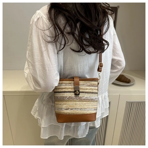 Détail d'un sac seau tissé avec garniture en cuir et fermoir doré porté par un modèle