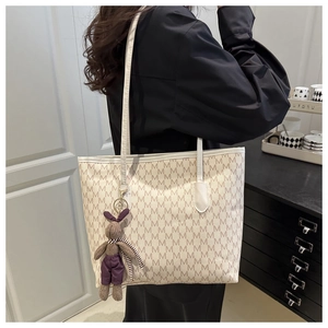 Detalle de bolso crema con patrón M y colgante de conejo de peluche morado lateral