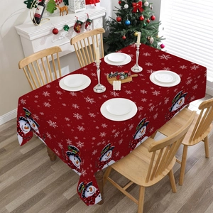 Red Christmas tablecloth with snowman and snowflake prints on a wooden dining table