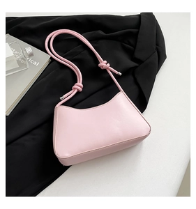 Detail of pink baguette bag with decorative knot strap on black blazer background