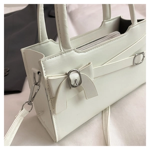 Detail view of white leather handbag with decorative bow buckle and detachable strap