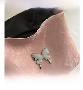 Gros plan du sac fourre-tout rose avec surface ondulée texturée et papillon en métal argenté