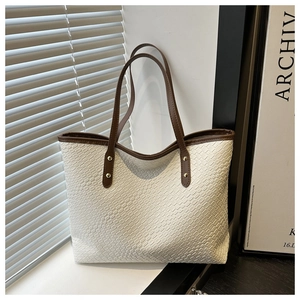Detail of woven white tote bag featuring brown leather handles and golden rivets