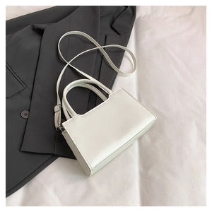 Detailed overhead view of a minimalist white square handbag resting on a grey blazer suit