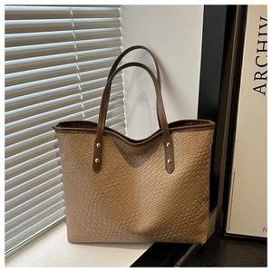 Detail of a brown embossed leather tote bag showing textured surface and gold rivets