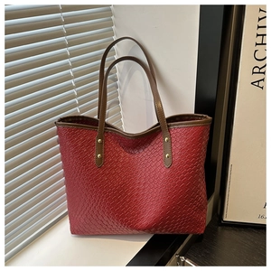 Detail of red woven tote bag featuring brown leather handle and gold rivet hardware