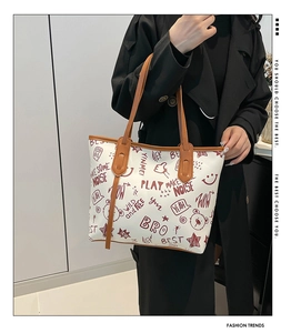 Detail of white tote bag with red graffiti print and brown leather handles on shoulder