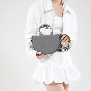 Borsa a mezzaluna grigia minimalista con manico in metallo argento su abito bianco