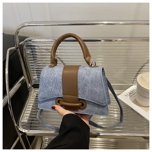 Detail of blue denim and brown leather handbag with adjustable crossbody strap