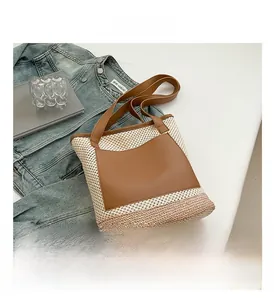 Detail view of woven straw tote bag with brown leather pocket and casual beach aesthetic