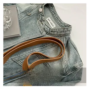 Macro detail of brown leather shoulder strap on a washed blue denim tote bag texture