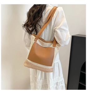 Detail of hollow woven straw tote with brown leather pocket and long shoulder strap